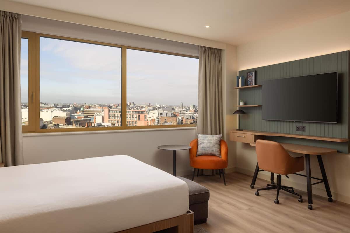 Ein Hotelzimmer mit Bett, Schreibtisch, Stuhl, Fernseher und Blick auf die Stadt.