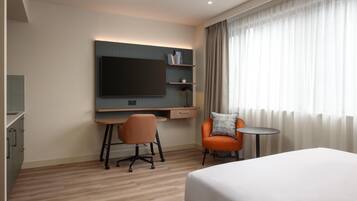A modern hotel room with a large bed, a desk with a chair, a television, and a small table.