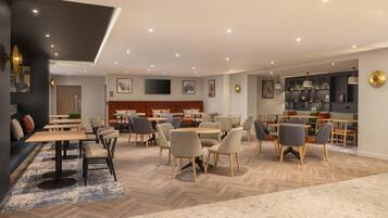 Un espace de restauration moderne, doté de plusieurs tables et chaises, d’un parquet en bois disposé en chevrons et d’un éclairage encastré au plafond.