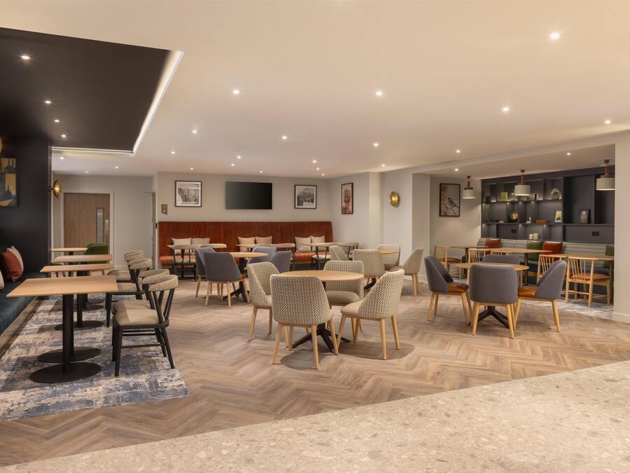 A modern dining area with multiple tables and chairs, a herringbone wood floor, and recessed ceiling lighting.