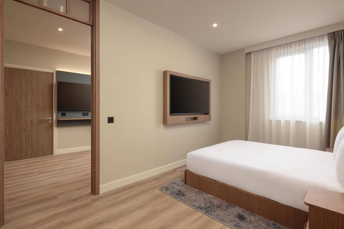 Ein Schlafzimmer mit Bett, einem Wand-Fernseher, einem Holzschrank und einer Badezimmertür.
