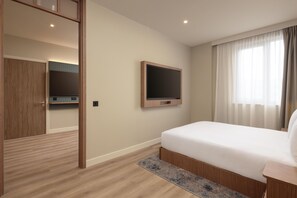 Une chambre à coucher avec un lit, un téléviseur fixé au mur, une armoire en bois et une porte menant à la salle de bain.