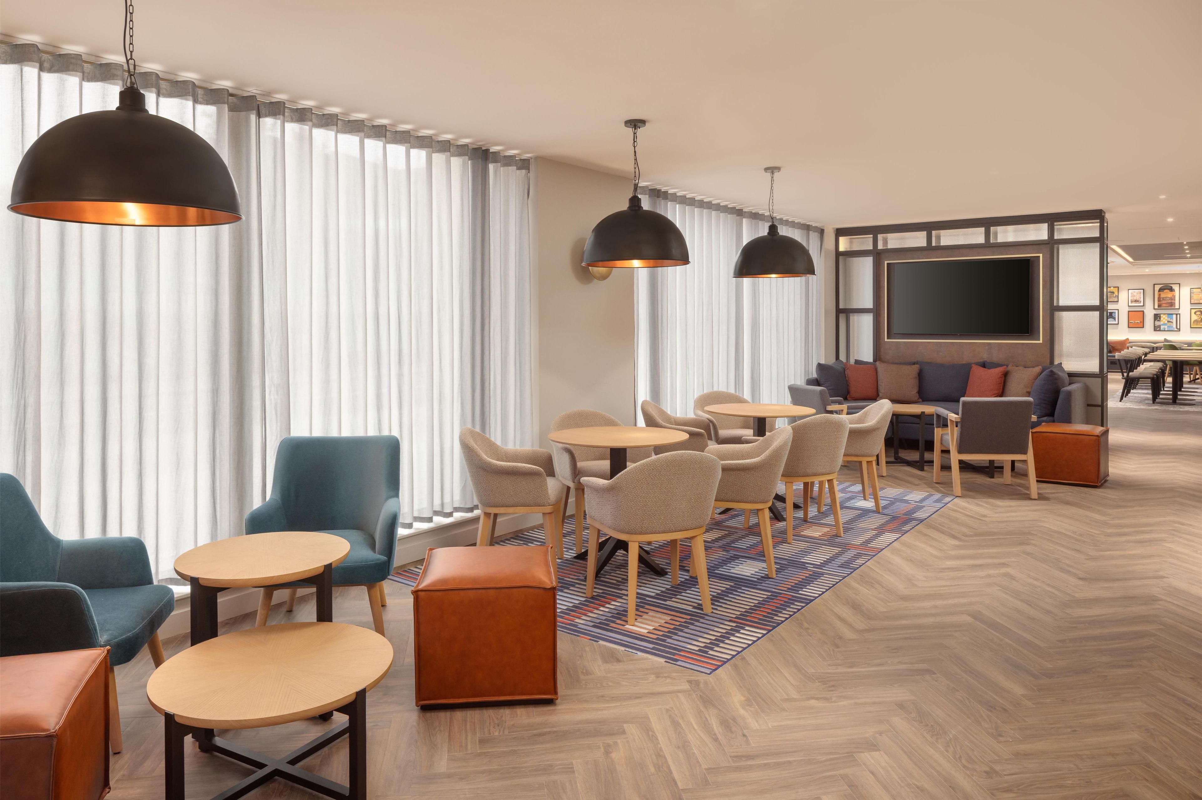 Een moderne hotelentree met een zithoek, grote ramen en een flatscreen televisie.