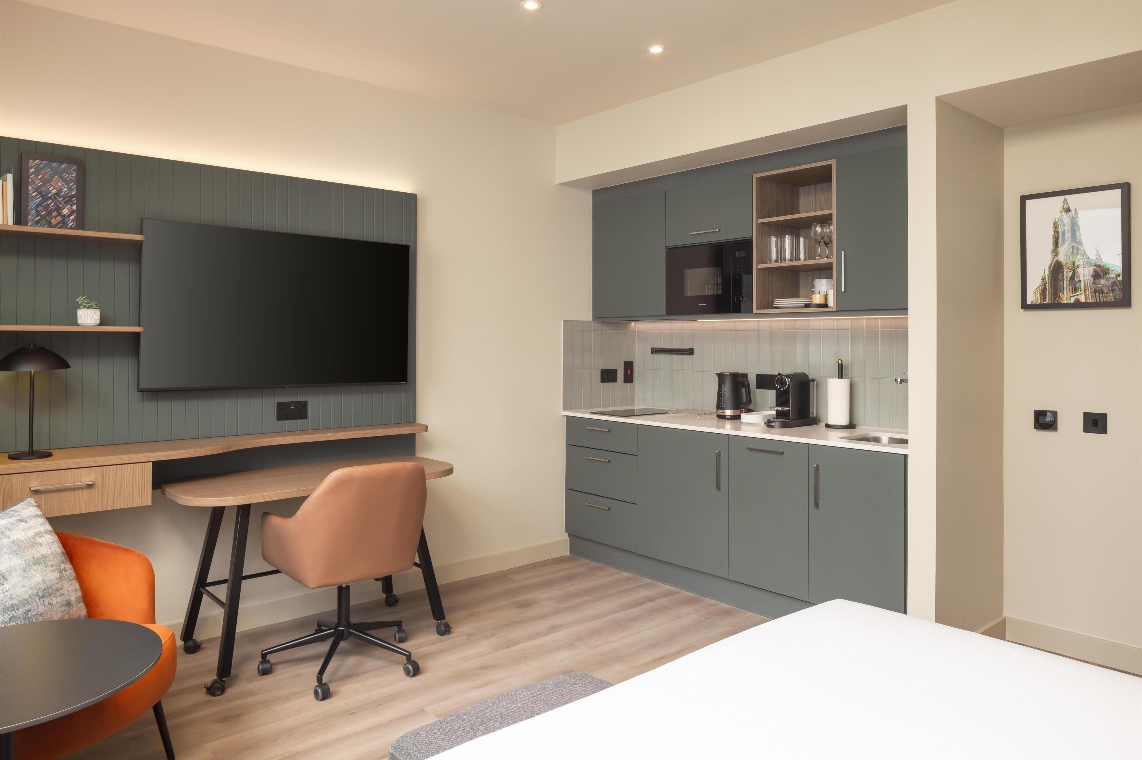 A modern kitchen with a flat-screen TV, a dining area with a table and chairs, and a workspace with a desk and chair.
