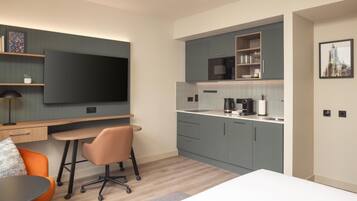 A modern kitchen with a flat-screen TV, a dining area with a table and chairs, and a workspace with a desk and chair.
