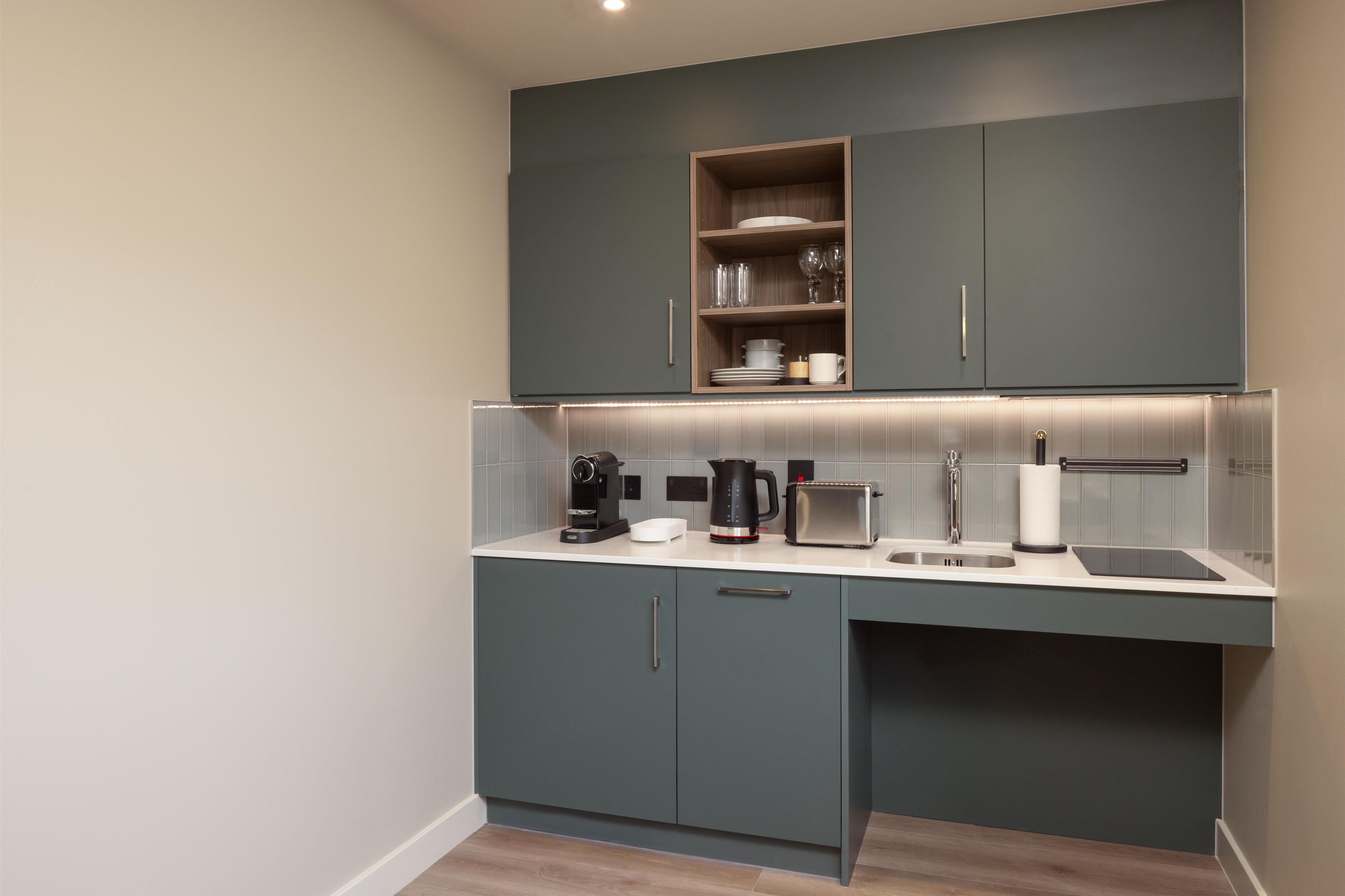 A modern kitchen with grey cabinets, a built-in shelf with glassware, a coffee maker, a toaster, and a sink.