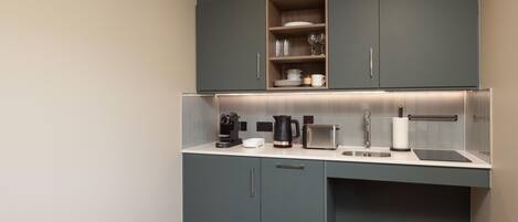 A modern kitchen with grey cabinets, a built-in shelf with glassware, a coffee maker, a toaster, and a sink.