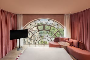 A bedroom with a large arched window, a flat-screen TV, a sofa, and a bed. - Hotel Palacio Bellas Artes San Sebastián, Curio Collection by Hilton (San Sebastián)