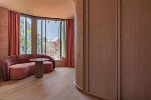 Een moderne kamer met een gebogen bank, een ronde tafel en grote ramen voorzien van gordijnen.