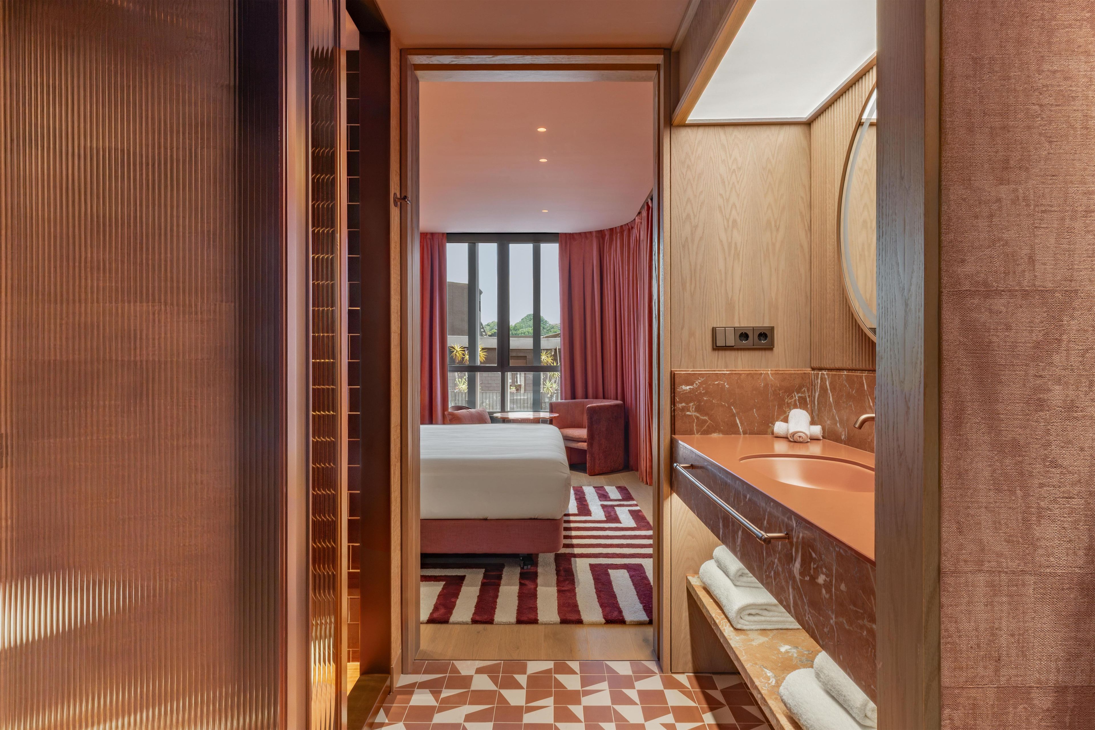 Een hotelkamer met een bed, een badkamer met een wastafel en spiegel, en uitzicht naar buiten.