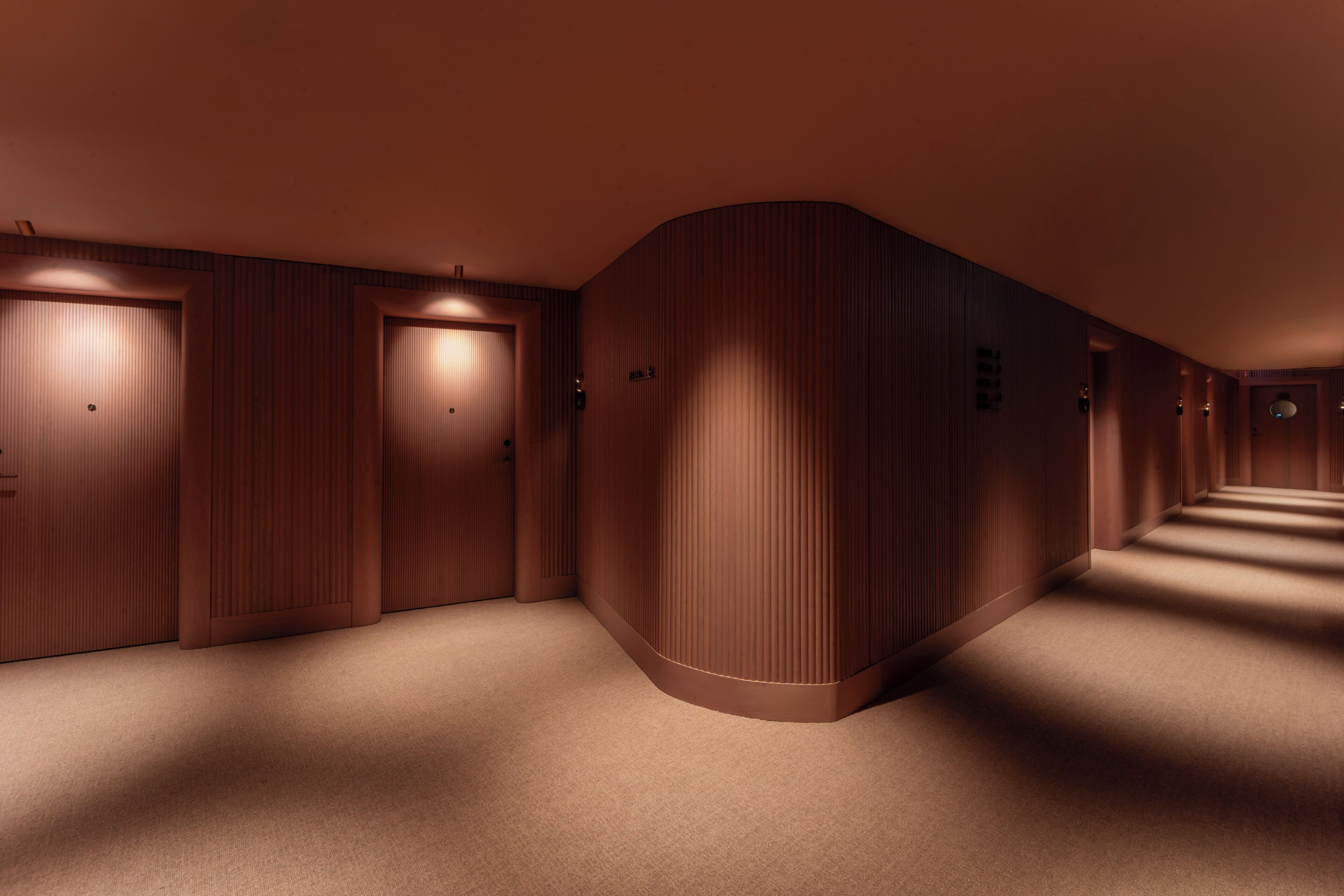 A hallway with wooden paneling and carpeted floors, leading to a set of doors.