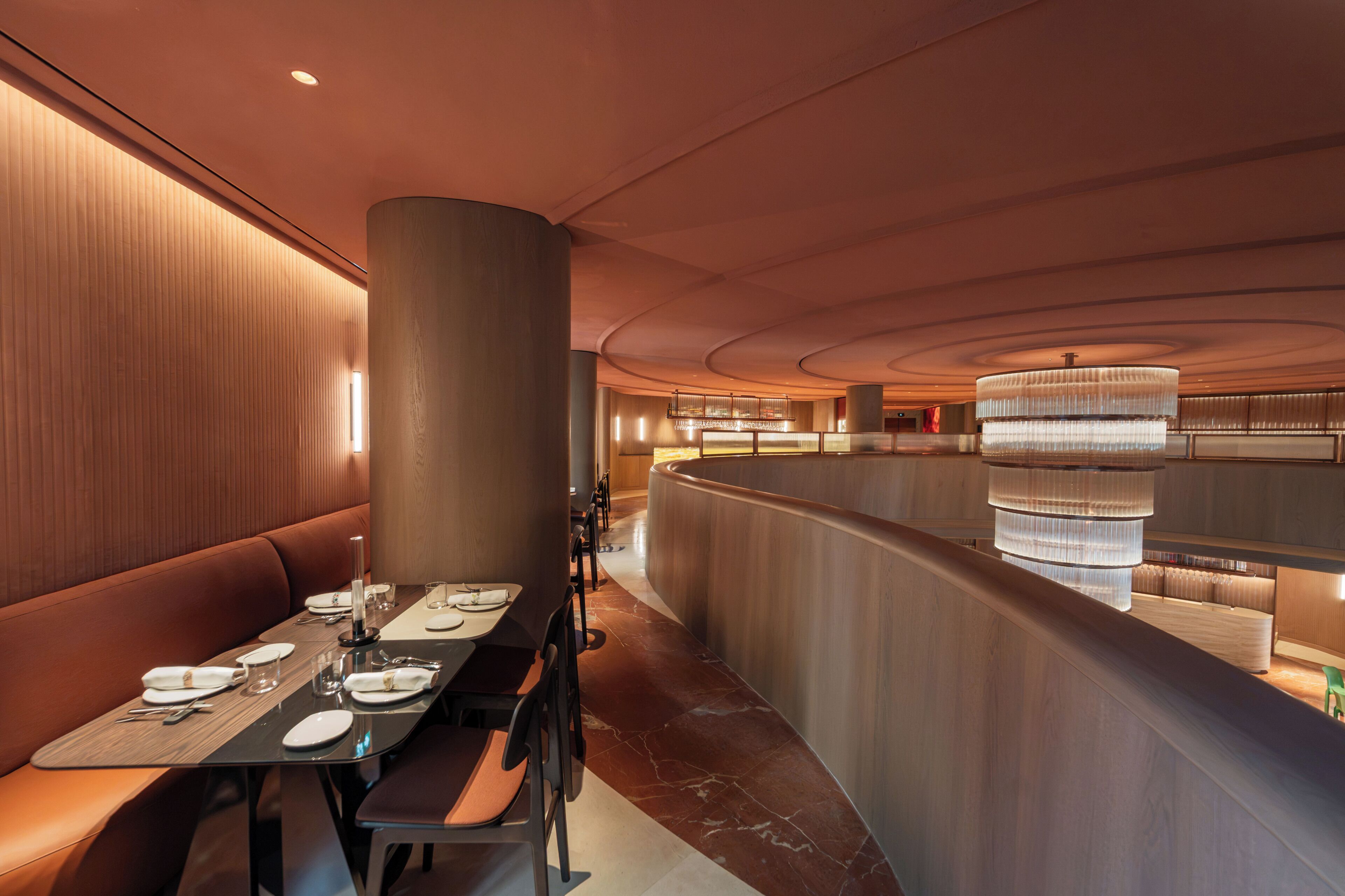 A modern restaurant with a curved seating area, a central column, and a chandelier.