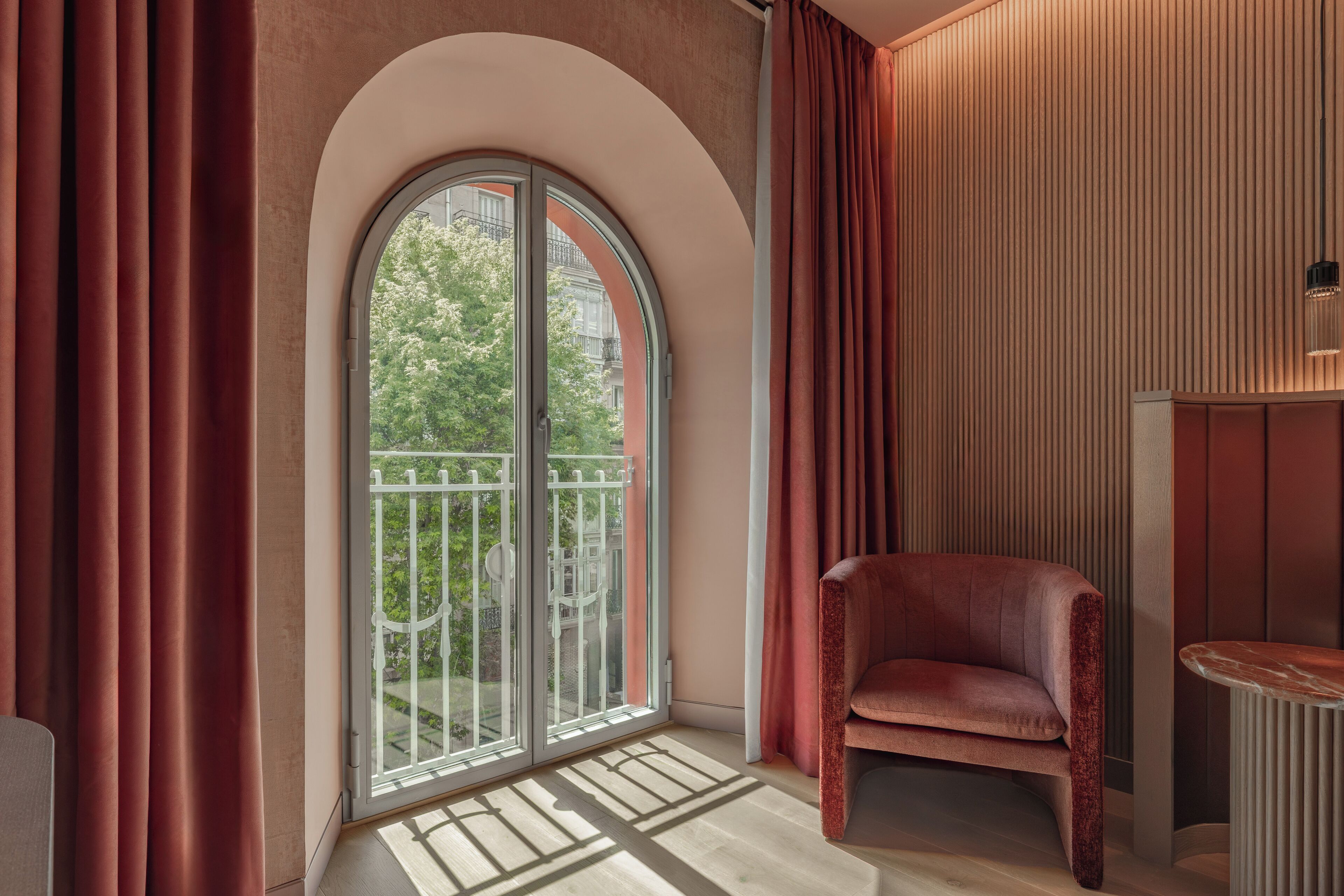 A room with a large arched window, a red chair, and a wooden panel wall.
