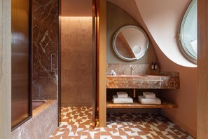Een badkamer met een marmeren wastafel, een ronde spiegel en een inbouwkastje met handdoeken.