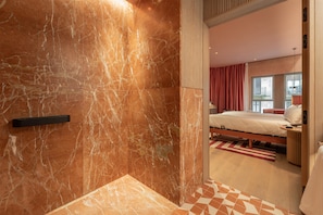 A hotel room with a marble wall, a bed, a bedside table, and a view of the city through the window. - Hotel Palacio Bellas Artes San Sebastián, Curio Collection by Hilton (San Sebastián)