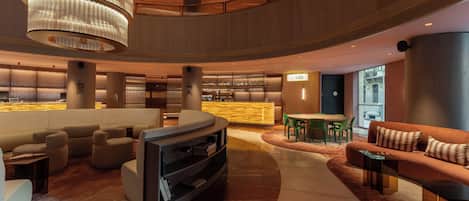 A modern lobby with a curved seating area, a bar, and a reception desk.