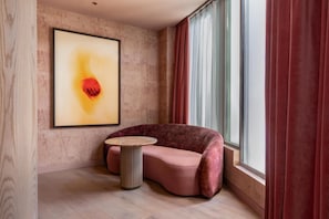 Una camera moderna con un divano curvo, un tavolino rotondo, un quadro astratto di grandi dimensioni e una finestra con tende.