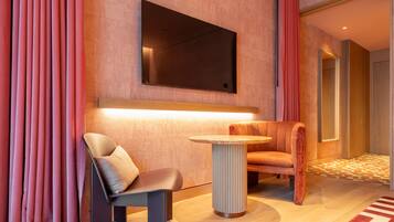 Een moderne hotelkamer met een bank, een stoel, een klein tafeltje, een flatscreen televisie aan de muur en een kamerbreed tapijt.