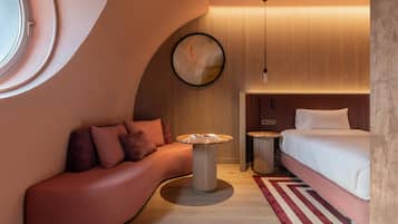 A modern hotel room with a curved sofa, a round table, a bed, and a large mirror.