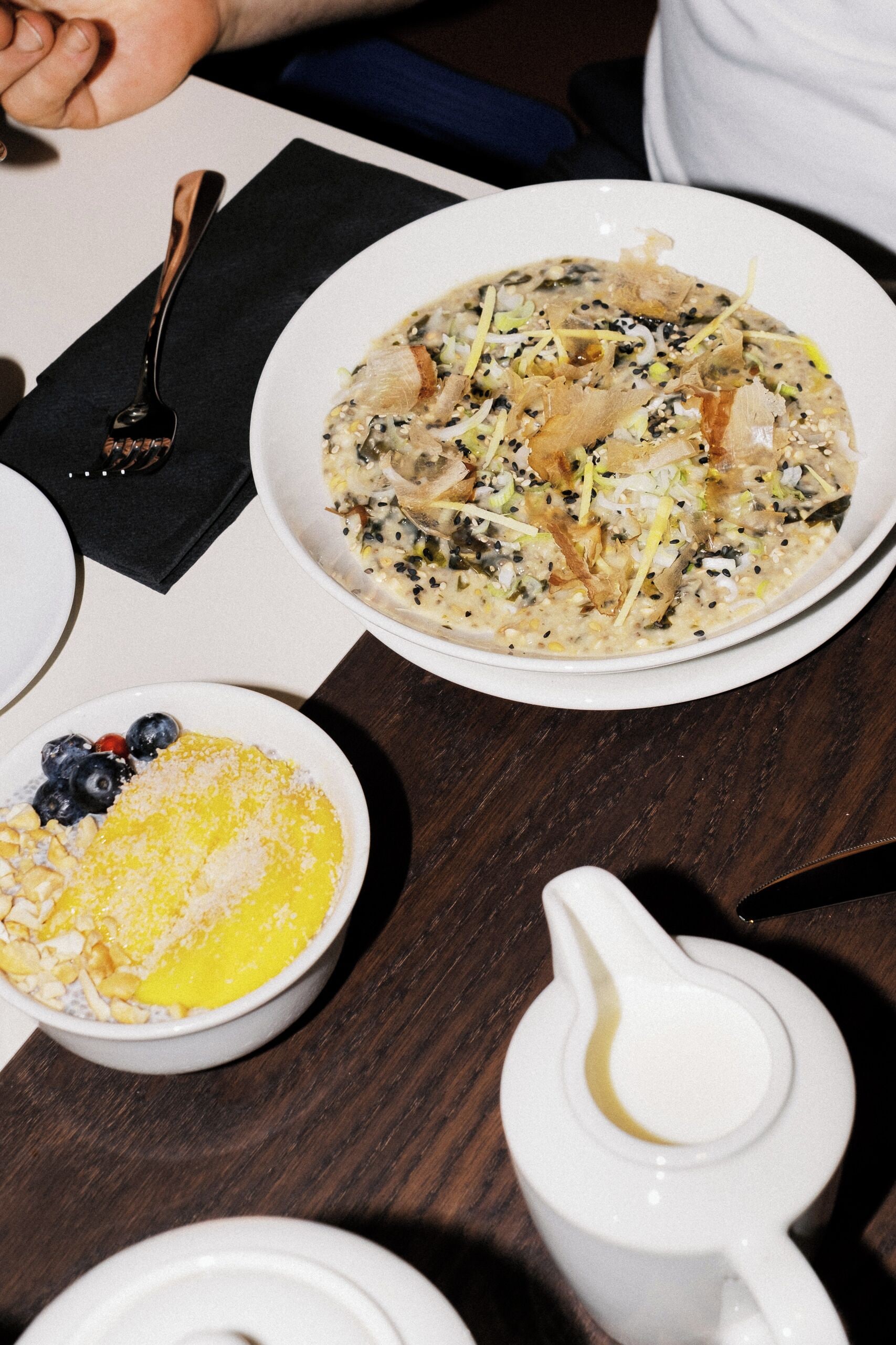 Une table à manger avec une assiette de nourriture, un bol de myrtilles et une carafe contenant un liquide jaune.