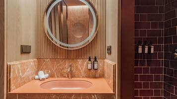 A bathroom with a marble sink, a round mirror, and toiletries on the wall.
