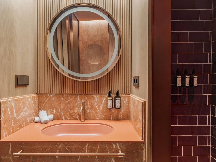 A bathroom with a marble sink, a round mirror, and toiletries on the wall.