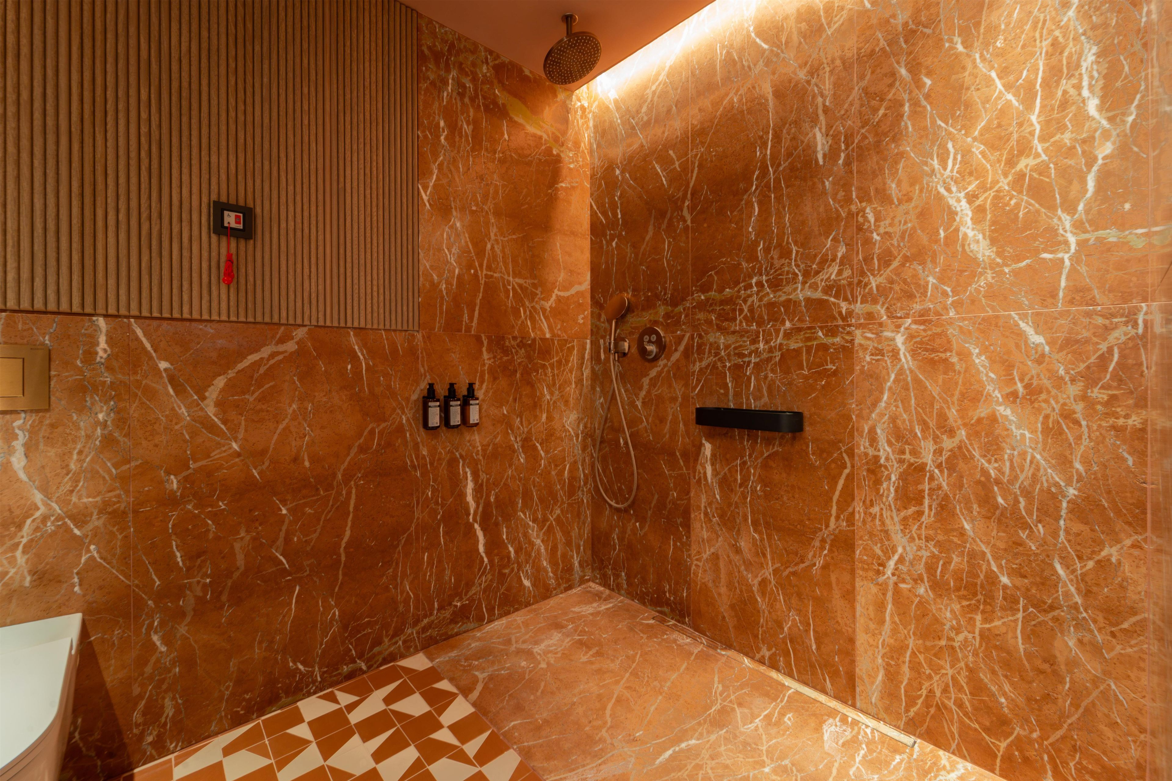 Un baño con pared de mármol, ducha y retrete.