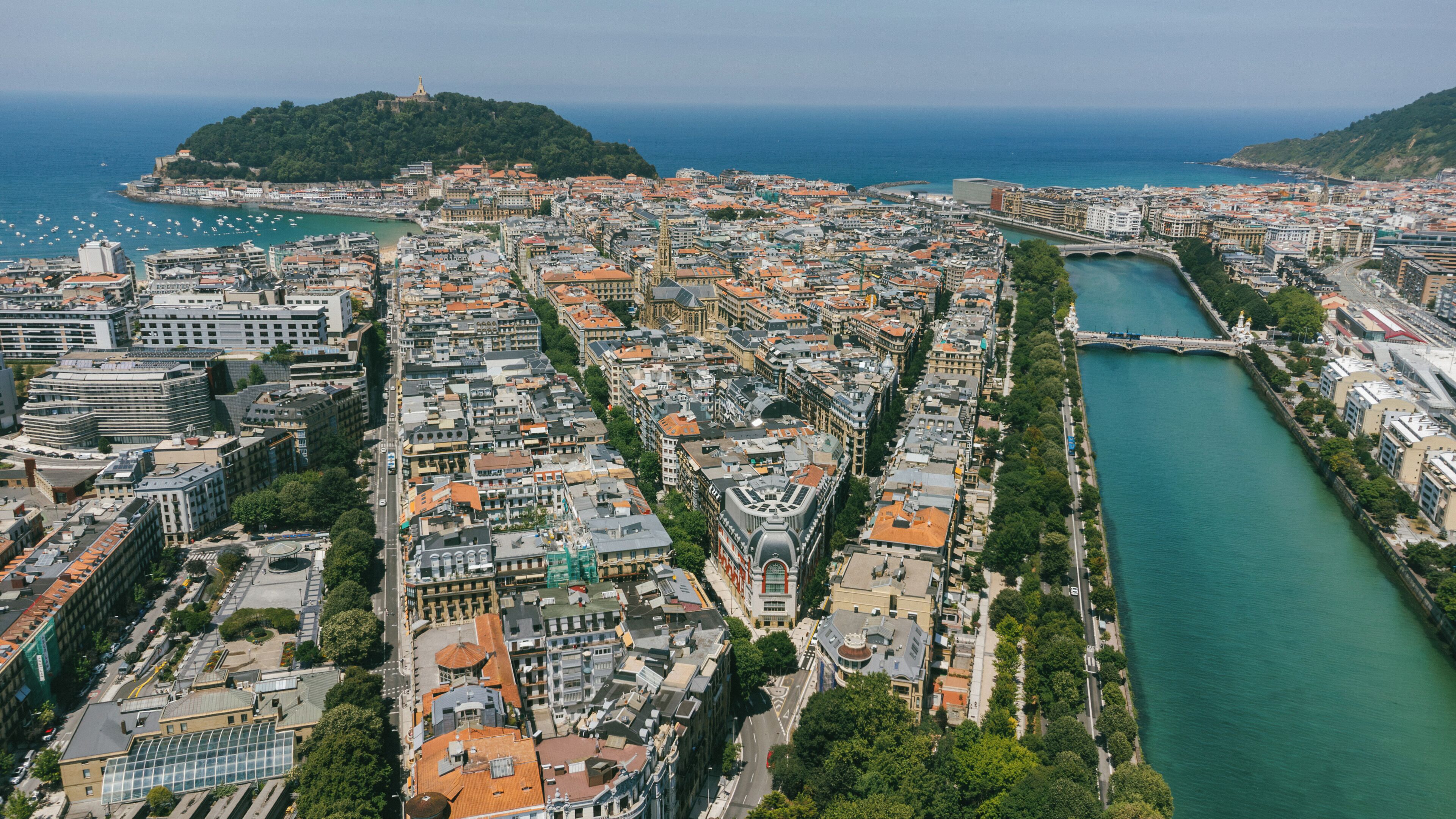 A coastal cityscape with a prominent river, dense urban buildings, and a hill with a fortification.