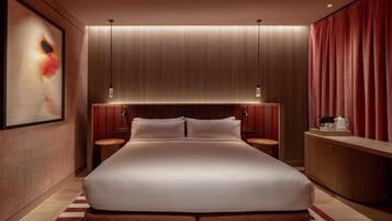A modern hotel room with a large bed, wooden headboard, two bedside tables, and a red curtain.