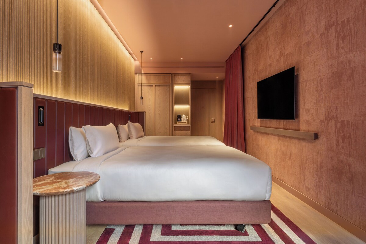 A modern hotel room with a large bed, a bedside table, a TV mounted on the wall, and a wooden panel design on the walls.