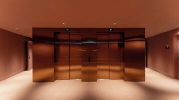 A modern elevator with a metallic finish, a carpeted floor, and wooden paneling on the walls.