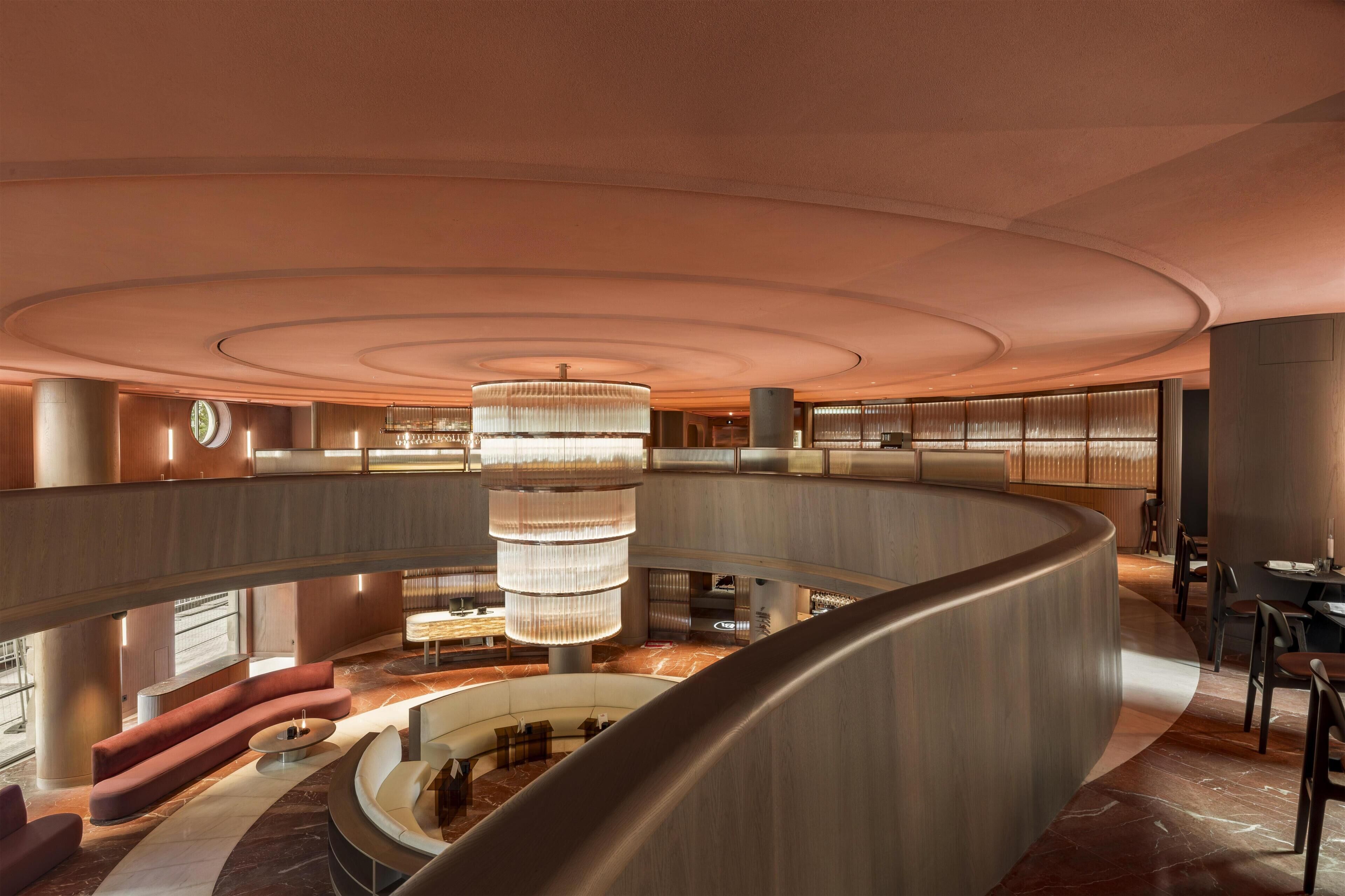 A spacious, modern lobby with a central chandelier, curved seating areas, and a mezzanine level.