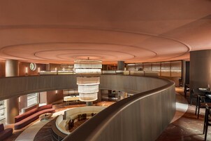 A spacious, modern lobby with a central chandelier, curved seating areas, and a mezzanine level.