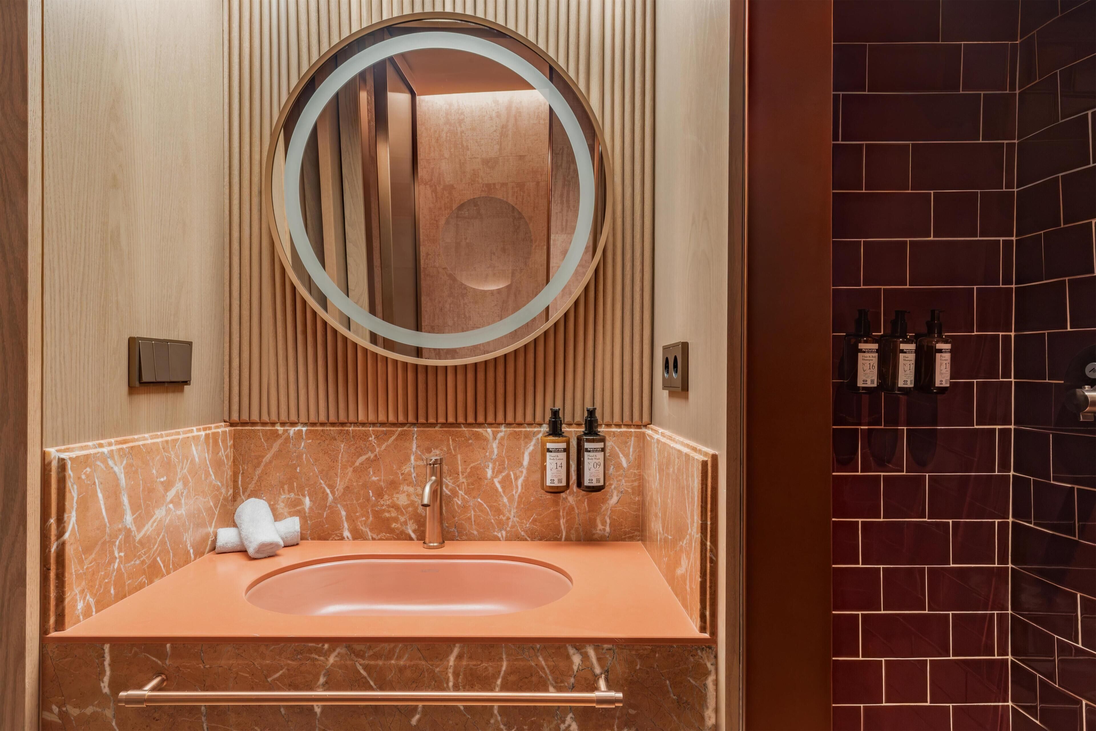 A bathroom with a marble sink, a round mirror, and toiletries on the wall.