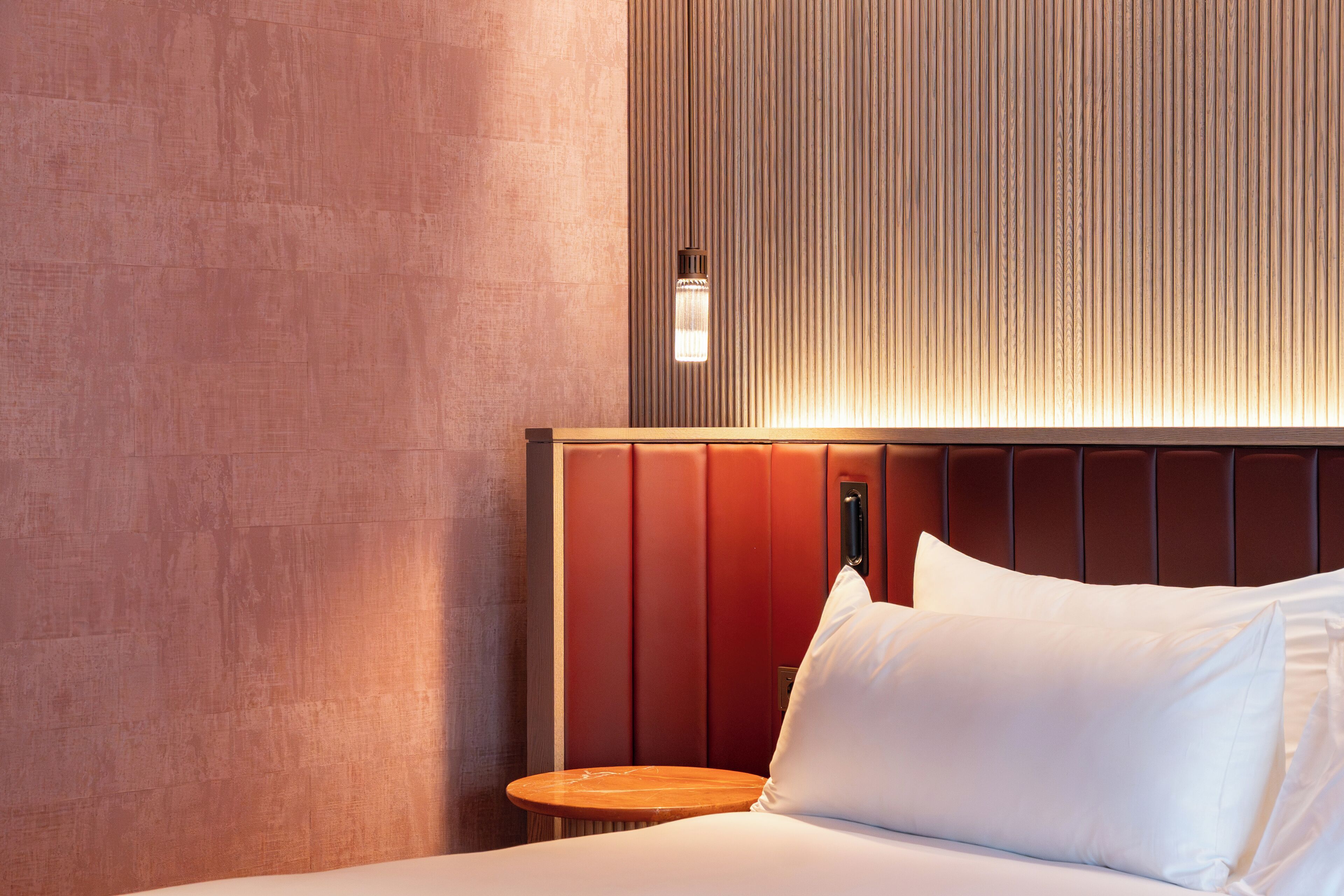 A hotel room with a bed, a nightstand, a wall-mounted light, and a textured wall.