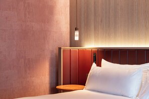 A hotel room with a bed, a nightstand, a wall-mounted light, and a textured wall. - Hotel Palacio Bellas Artes San Sebastián, Curio Collection by Hilton (San Sebastián)