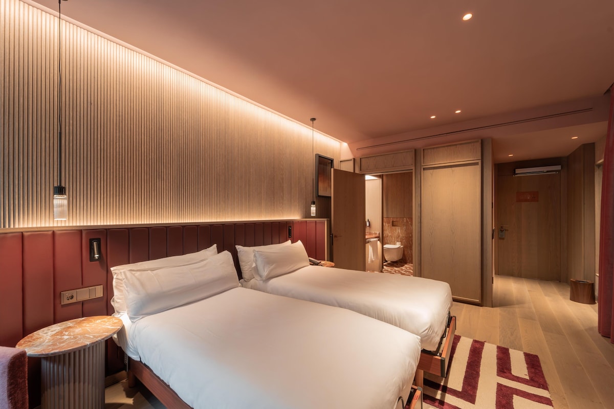 A hotel room with two beds, a bedside table, a mirror, and a wardrobe.