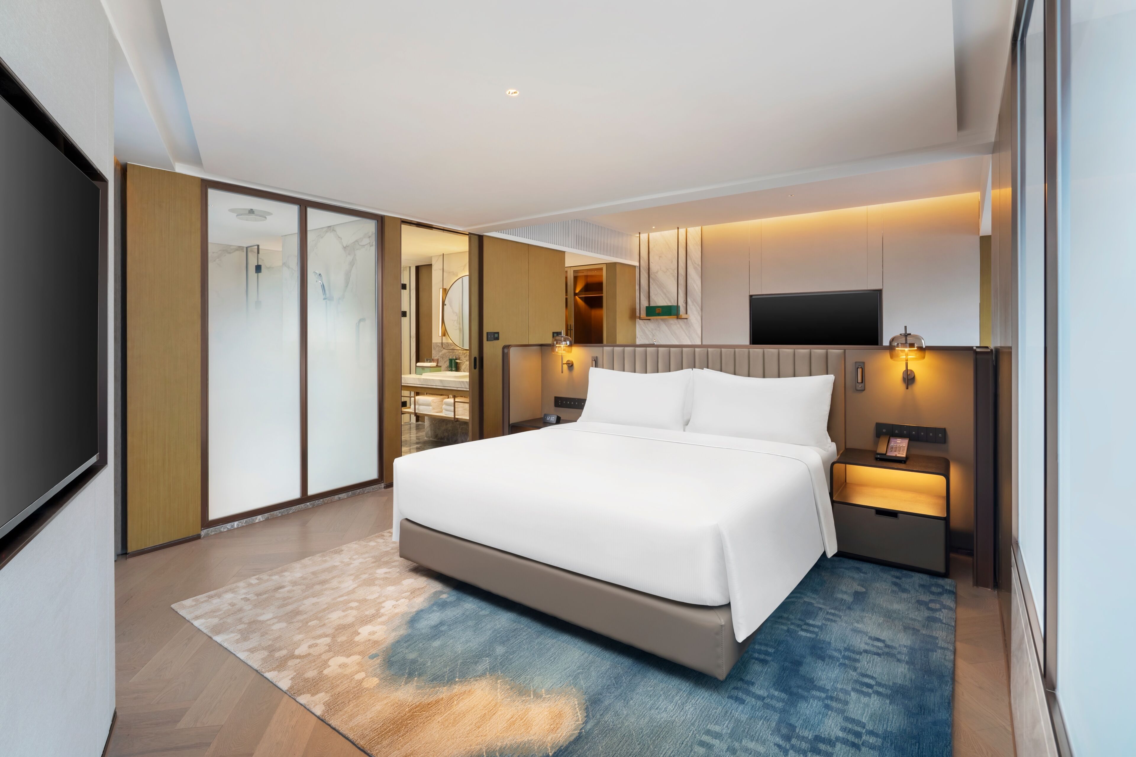 Een moderne hotelkamer met een groot bed, een flatscreen televisie, een nachtkastje en een badkamer die zichtbaar is door een schuifdeur.