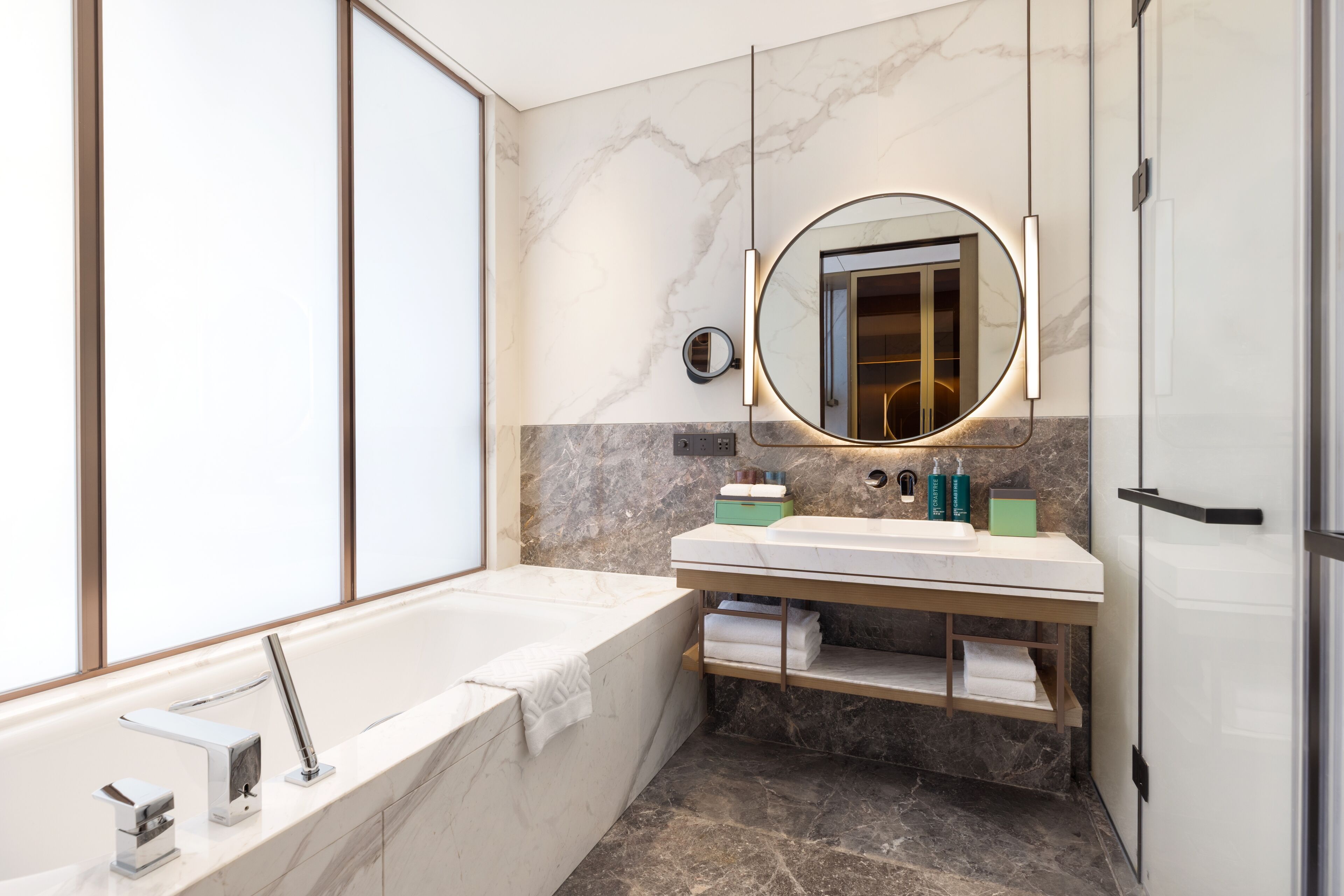 Un baño moderno con bañera, tocador con espejo y paredes de mármol.