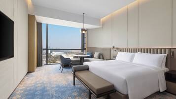 A hotel room with a large bed, a bench, a desk, and a view of the city.