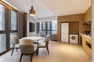 Una cocina moderna con lavadora y secadora integradas, un comedor con mesa redonda y sillas, y ventanas amplias que ofrecen luz natural.
