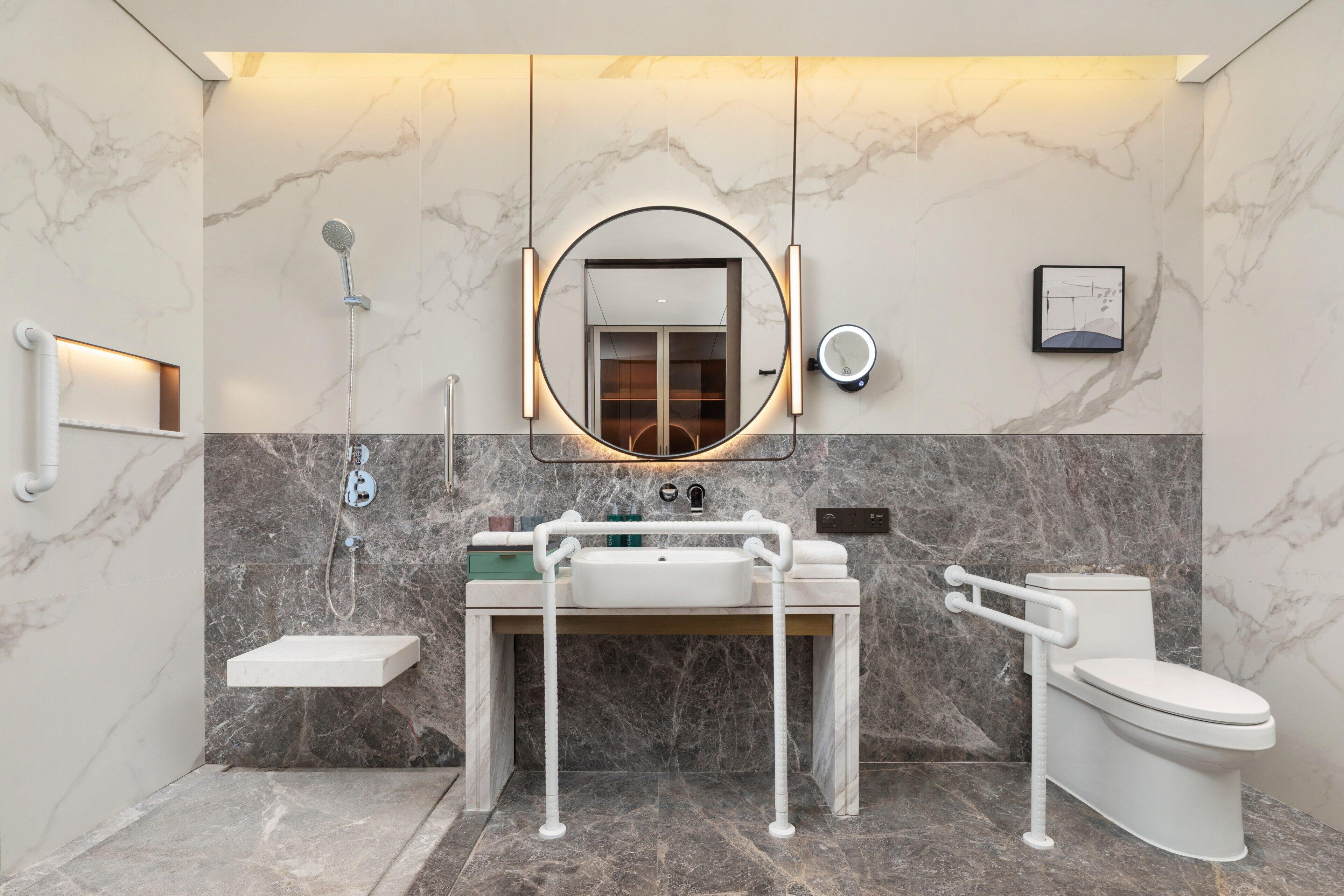 A modern bathroom with a marble wall, a round mirror, a sink, a toilet, and a shower.