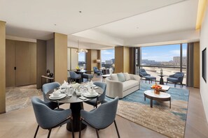 Une chambre d’hôtel moderne dotée d’un coin repas, d’un espace de vie avec un canapé et des fauteuils, et d’un balcon offrant une vue sur la ville.