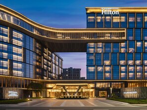 A modern hotel with a curved facade, large windows, and a prominent entrance. - Hilton Shaoxing Hotel And Residences (Shaoxing)