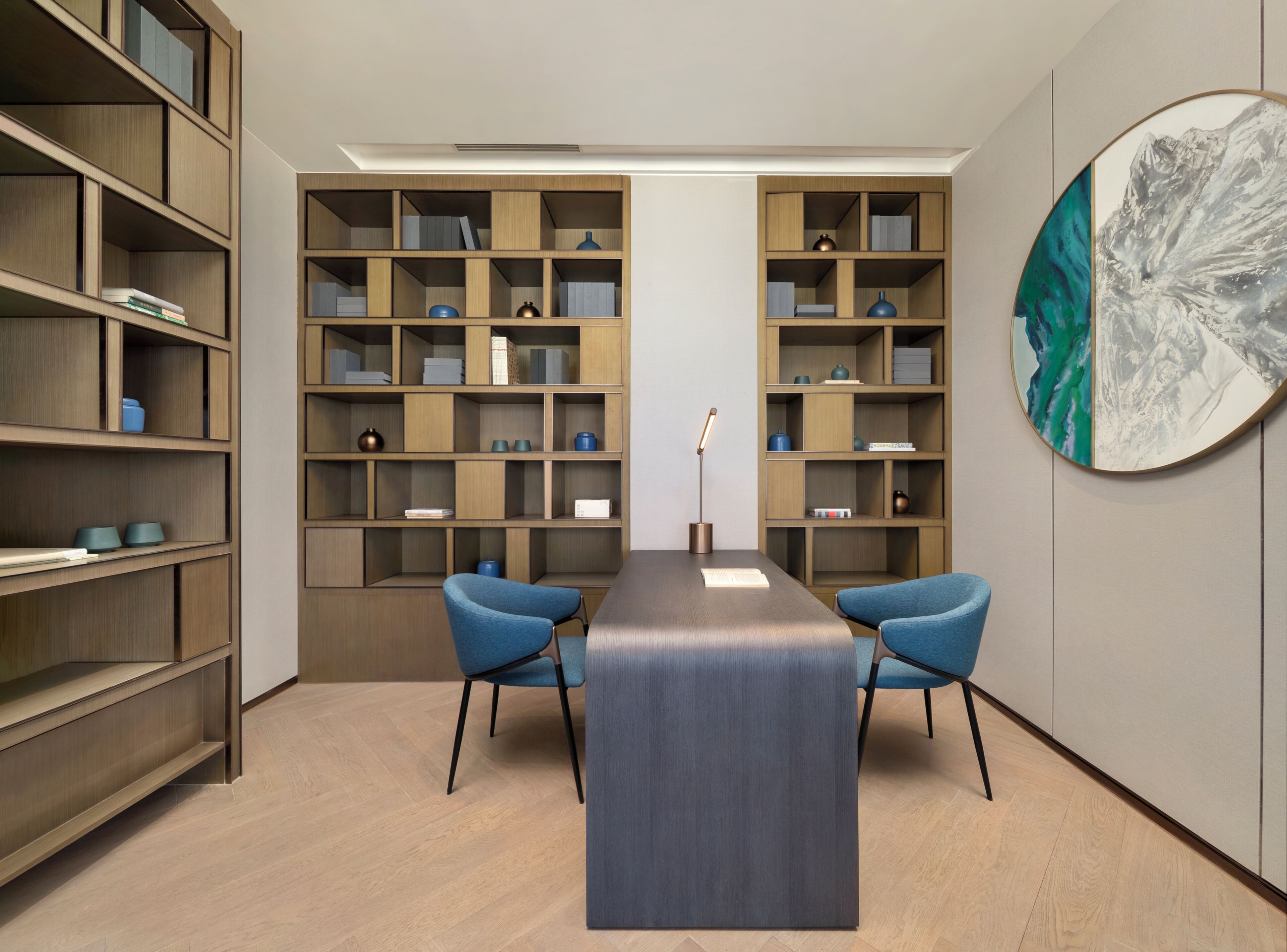 Quarto moderno com uma mesa central, duas cadeiras azuis e estantes de madeira embutidas.