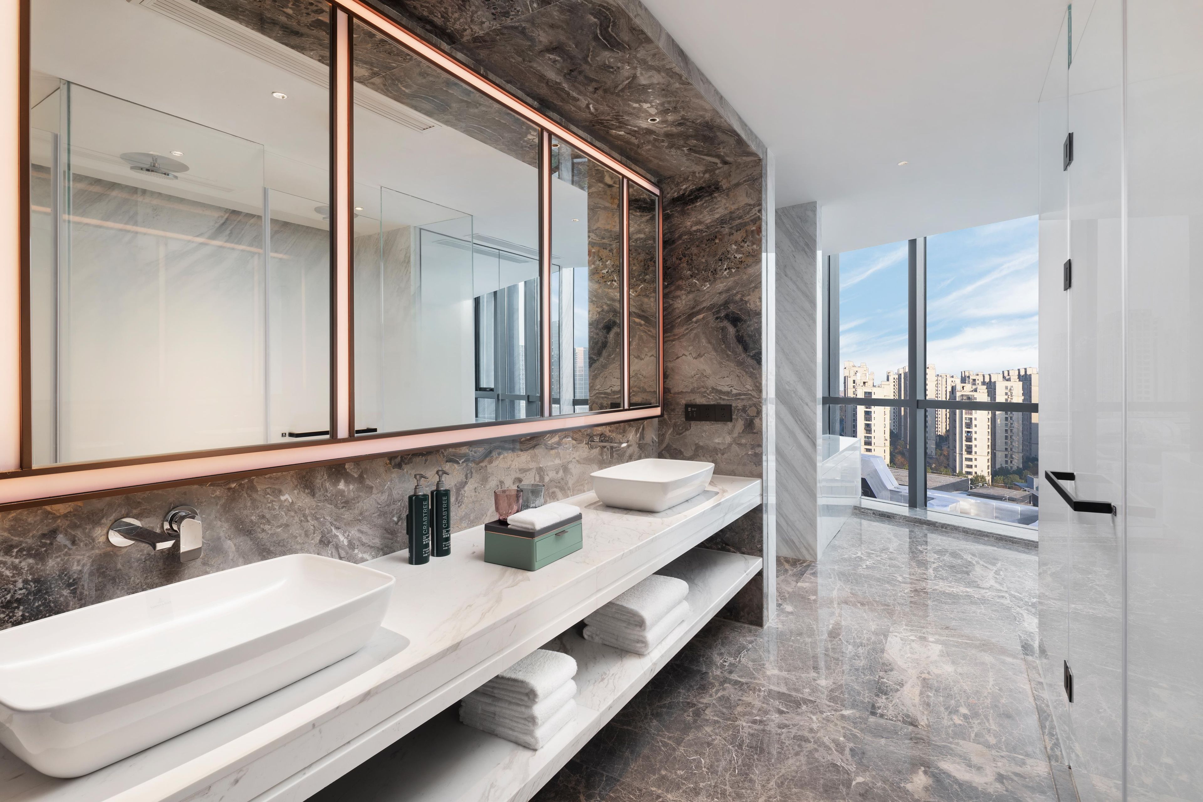 Uma casa de banho moderna com um espelho grande, duas lavatórios e vista para a cidade.