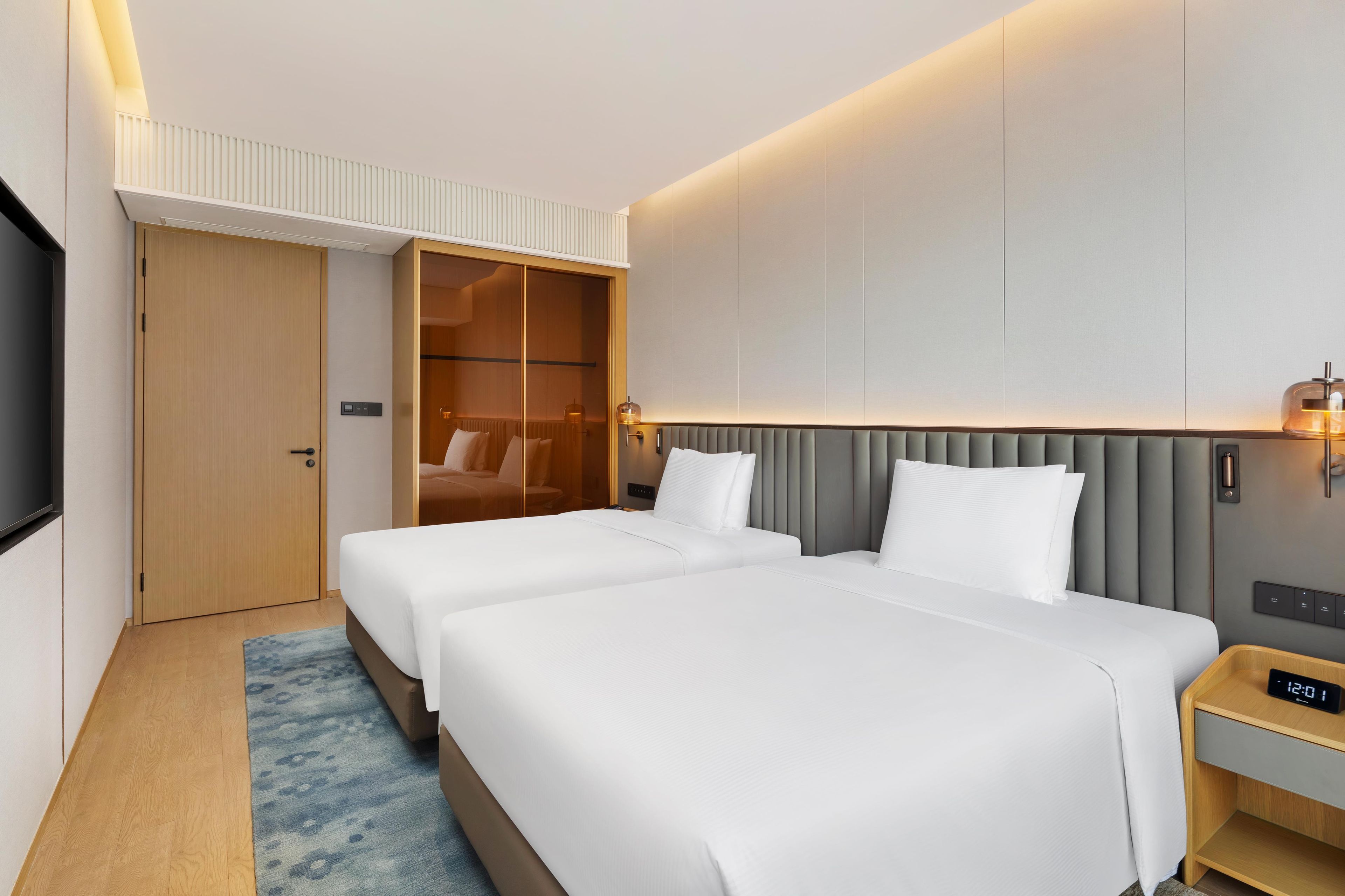 Habitación de hotel con dos camas, un armario, un televisor y una mesita de noche con un reloj digital.