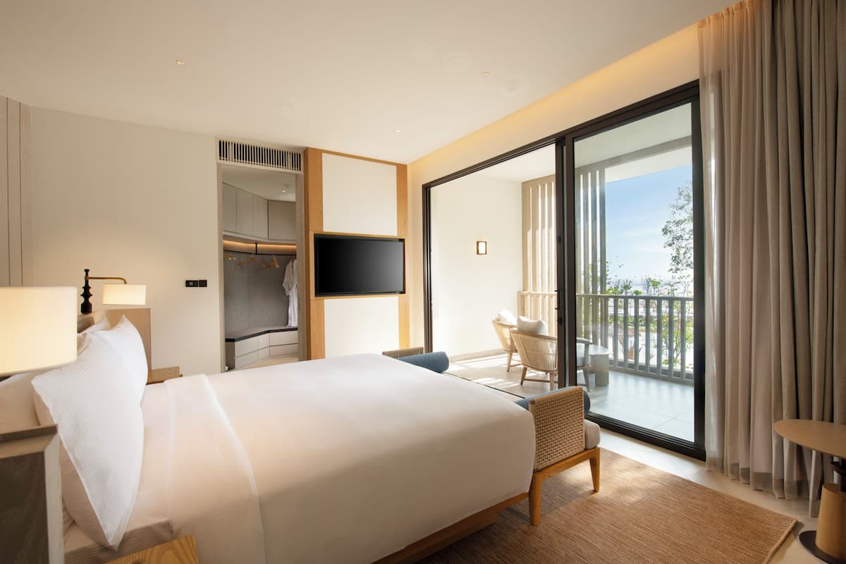 Habitación de hotel con cama, televisor, balcón con vistas y zona de estar.