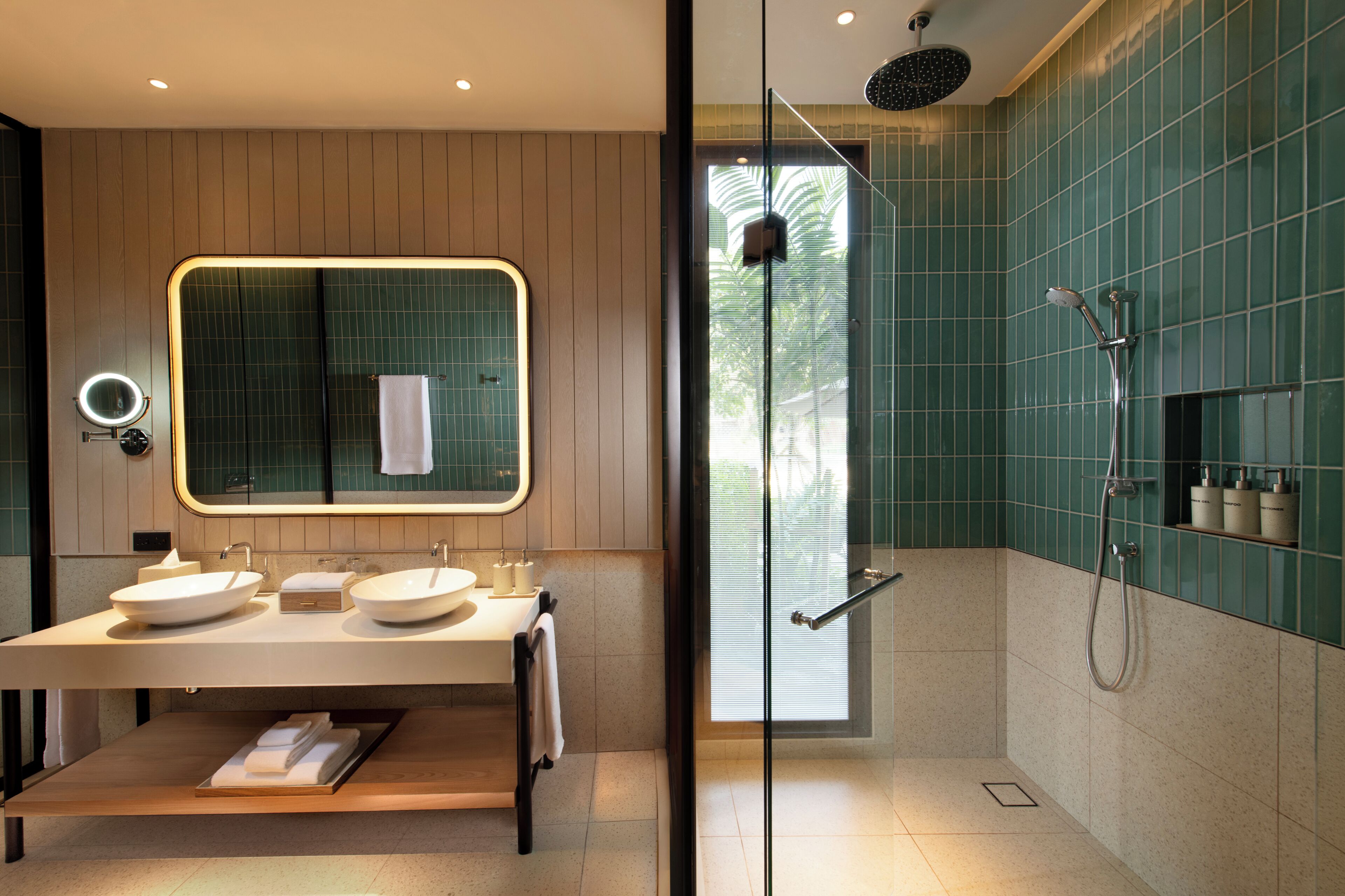 Un baño moderno con ducha de vidrio, dos lavamanos, un espejo grande y un perchero para toallas.