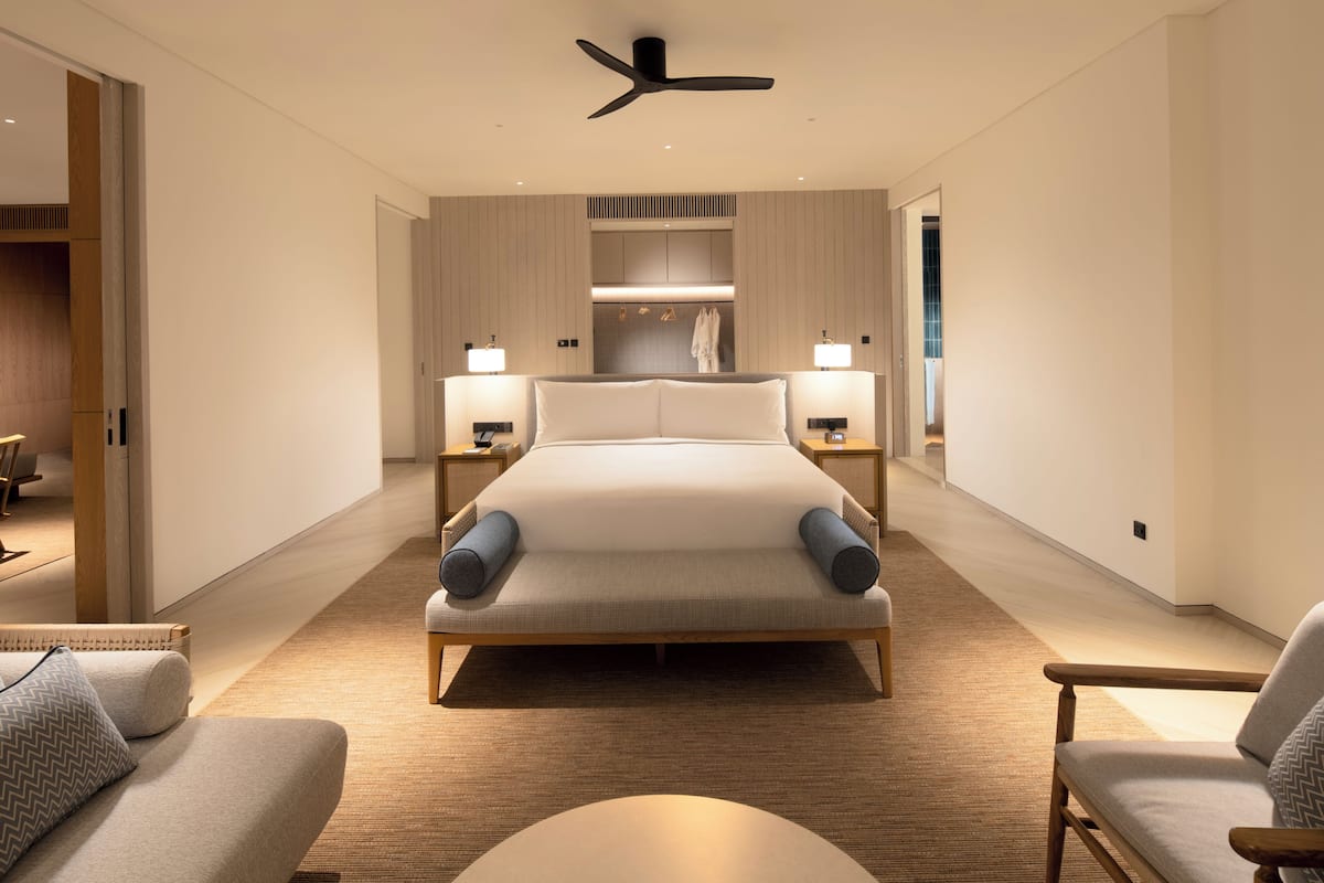 Une chambre d’hôtel moderne avec un grand lit, des lampes de chevet, un ventilateur de plafond et une vue sur la salle de bain.